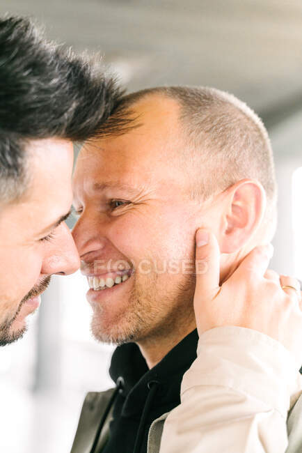 Side view of happy young multiracial gay couple hugging and looking at each other on street on sunny day — Foto stock