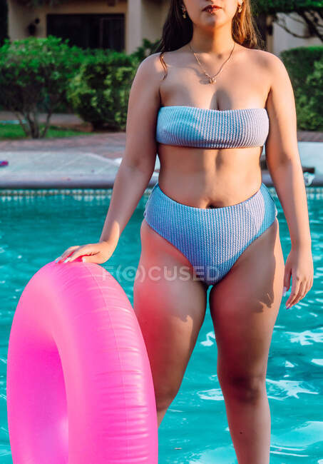 Кукурудза невизначена пухнаста жінка-туристка в купальнику з надувним кільцем, що стоїть проти басейну під час літніх канікул — стокове фото