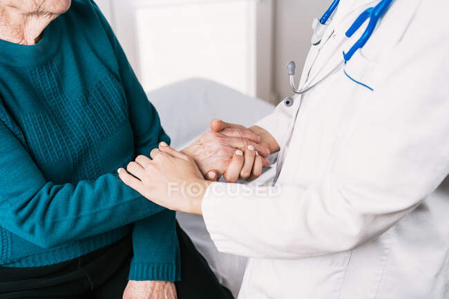 Crop anonymous doctor speaking with elderly woman while holding hands during examination in hospital — Stock Photo