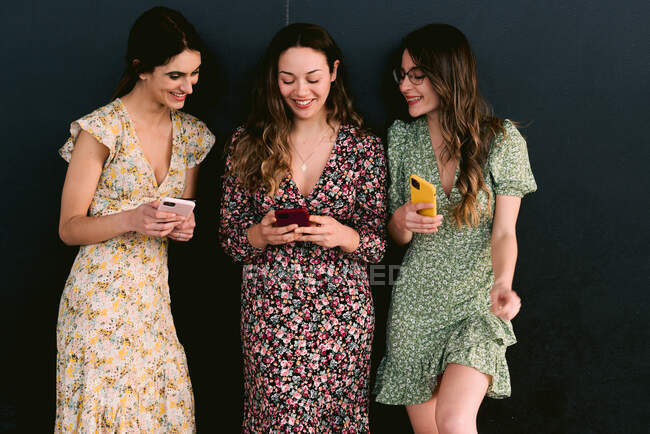 Задовольняйте молодих кращих подруг модним одягом з мобільними телефонами, що стоять на міській доріжці до стіни. — стокове фото