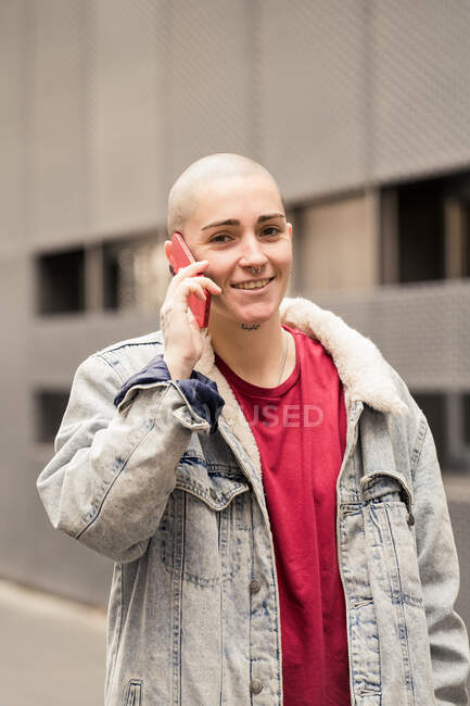 Transgender person in casual apparel talking on cellphone while looking at camera against urban building in daylight — Stock Photo