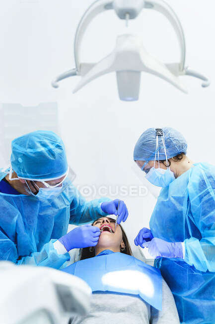 Анонімний стоматолог зі співробітником стерильної форми, що лікує зуби жінки з професійними інструментами на стоматологічному стільці в клініці. — стокове фото