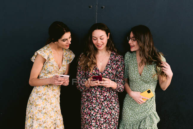 Contenuto giovani migliori amiche in abbigliamento alla moda con i telefoni cellulari in piedi sulla passerella urbana contro il muro — Foto stock