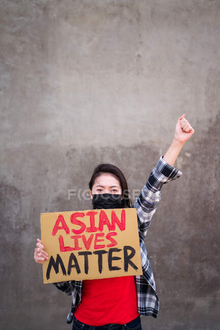 Donna etnica in maschera e con cartello di cartone con iscrizione Asian Lives Matter che protesta con braccio alzato in strada e guarda la macchina fotografica — Foto stock