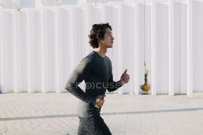 Side view of energetic man in black sportswear sprinting on paved road of industrial city district — Stock Photo