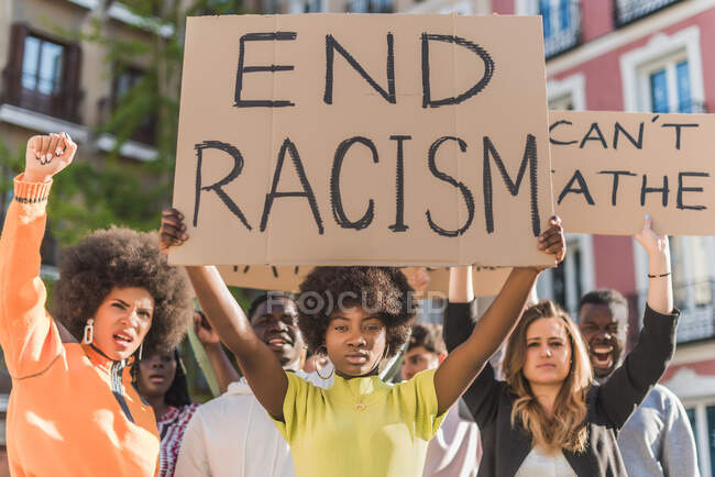 African American female activist with afro hair standing with End Racism poster standing on city street during Black Lives Matter protest looking at camera — Stock Photo