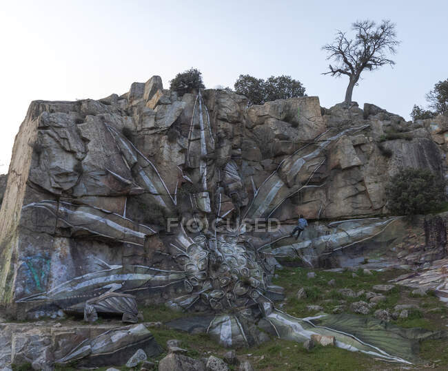 Вид на безпілотника, який висить на мотузці під час малювання графіті на крутому кам'яному схилі — стокове фото