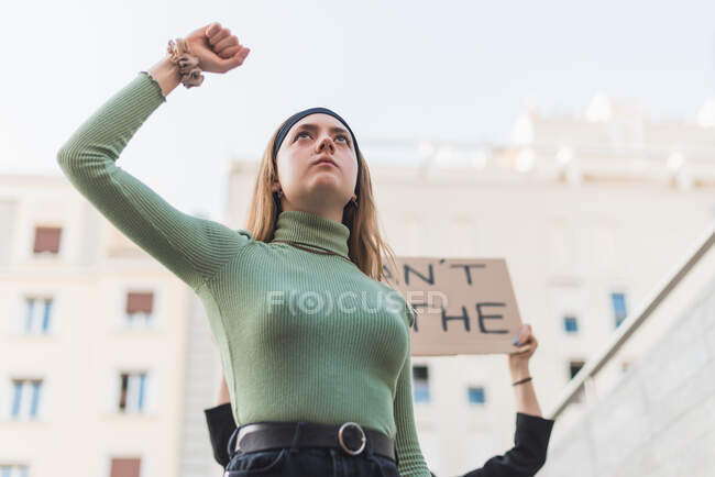 From below of caucasian female activist standing with fist up on street and protesting against racial discrimination during Black Lives Matter demonstration - foto de stock