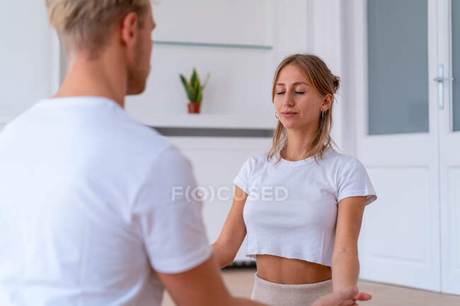Peaceful couple sitting in Lotus pose and holding hands while practicing yoga together and meditating with closed eyes — Stock Photo
