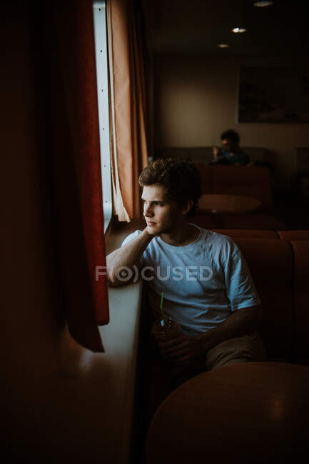 Вид сбоку вдумчивый молодой мужчина в повседневной летней одежде сидит на мягком диване во время путешествия на пароме по волнистому морю в Греции ярко — стоковое фото