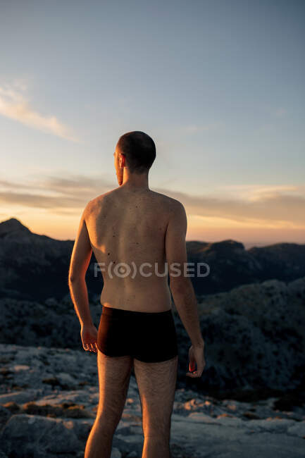 Back view anonymous male hiker in black underpants standing on rocky mountain summit and admiring spectacular highlands scenery at sunset — Stock Photo
