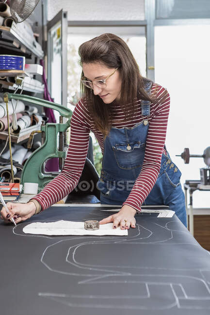 Sonríe mujer marcando pieza de cuero negro mientras crea tapicería para asientos de motocicleta en el taller juntos - foto de stock