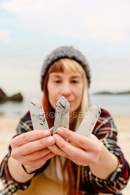 Creative female artisan showing collection of white semiprecious stones to camera on background of sea — Stock Photo