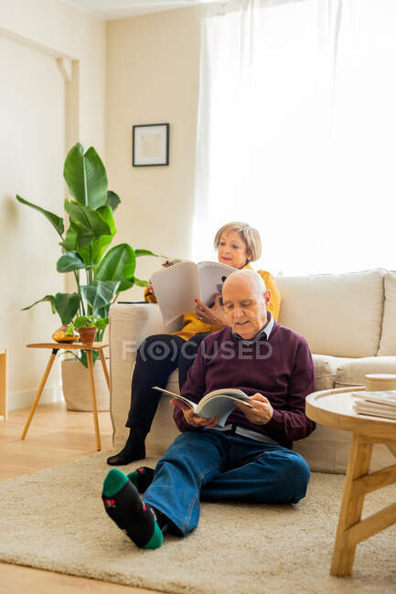 Молоді люди середнього віку сидять у затишній вітальні й читають книжки під час вихідних. — стокове фото
