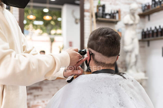 Crop anonymen männlichen Stylisten mit Trimmer schneiden Haare der Kundin in Umhang in Friseursalon — Stockfoto