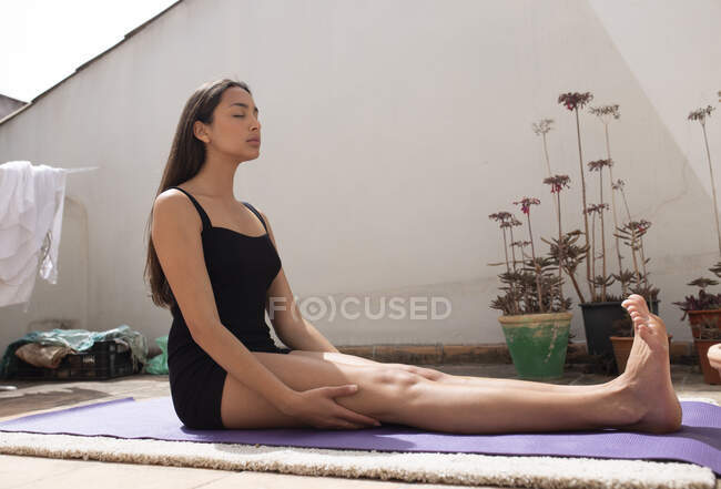 Повна довжина босоніж жінка сидить на йога килимок з закритими очима на сонячному балконі і роздумуючи — стокове фото