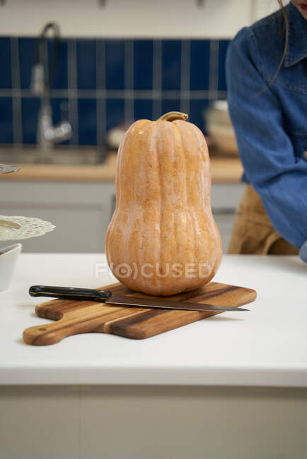 Ritaglio femminile irriconoscibile a tavola con zucca fresca e coltello sul tagliere in cucina di casa — Foto stock