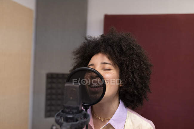 Cantante nera che canta contro il microfono con filtro pop in piedi e gli occhi chiusi sullo studio sonoro — Foto stock