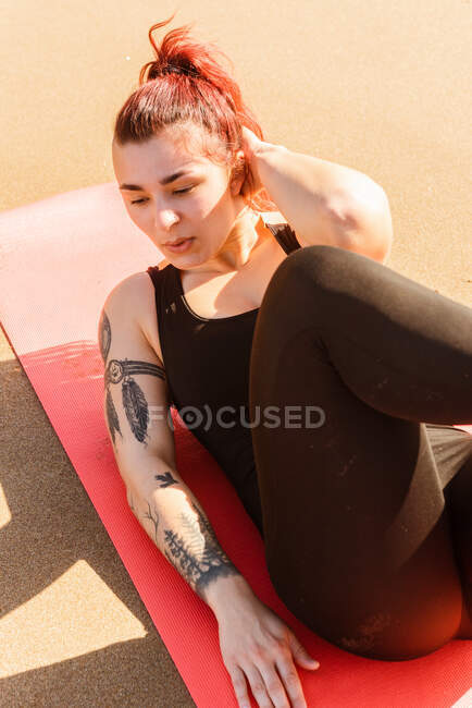 From above of adult female athlete in sports clothes pumping press while breathing and looking away on sandy beach — Stock Photo