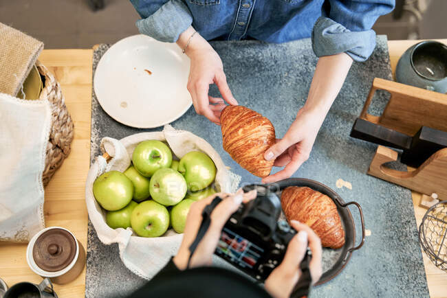 From above of crop anonymous female taking photo of delicious pastry on camera against girlfriend at kitchen table — Stock Photo