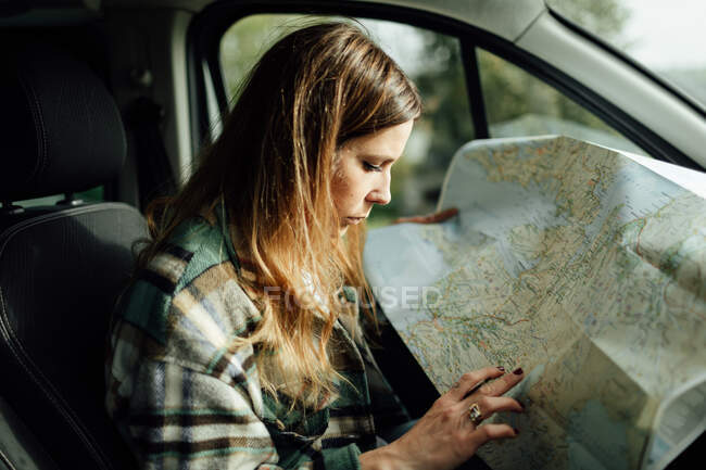 Seitenansicht einer fokussierten Touristin, die sich im Auto Notizen auf der Routenkarte macht — Stockfoto