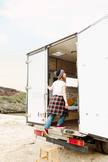 Вид збоку на жіночого мандрівника, що входить у фургон, припаркований на піщаному березі у високогір'ї під час поїздки — стокове фото