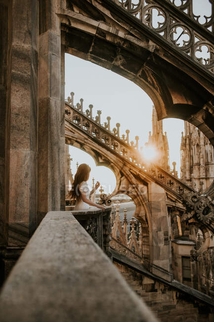 Side view of unrecognizable female traveler admiring Milan from stone balcony of aged church in sunshine in Italy — Stock Photo