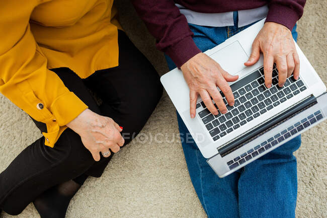Visão superior da colheita casal maduro anônimo sentado no chão em casa e netbook de navegação juntos — Fotografia de Stock