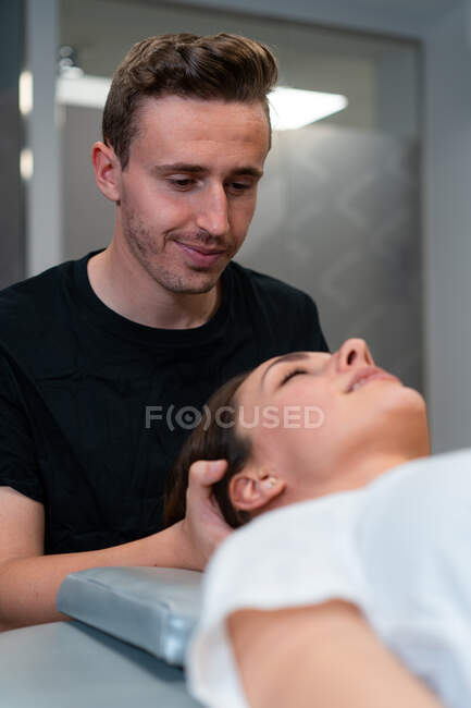 Fisioterapeuta masculino sin afeitar masajeando cuello de mujer con los ojos cerrados en el hospital - foto de stock
