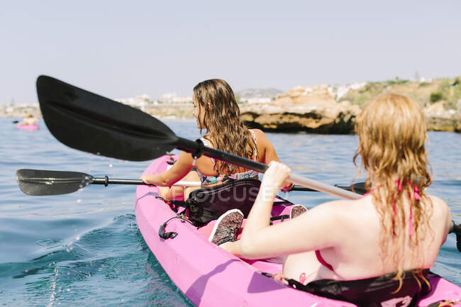 Back view travelers with paddles floating on turquoise seawater near the rocky shore on sunny day in Malaga Spain — Stock Photo