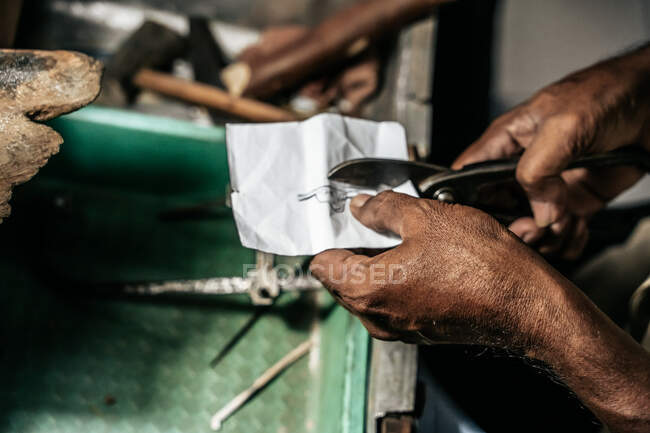De arriba la cosecha el maestro étnico con las tijeras que cortan la plantilla de papel de la joyería futura en el taller - foto de stock