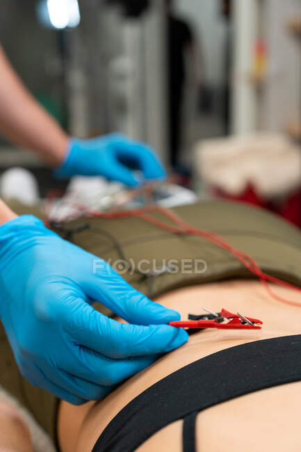 Обрезать неузнаваемого физиотерапевта в стерильных перчатках, вставить электрод иглы в заднюю кожу женщины в больнице — стоковое фото