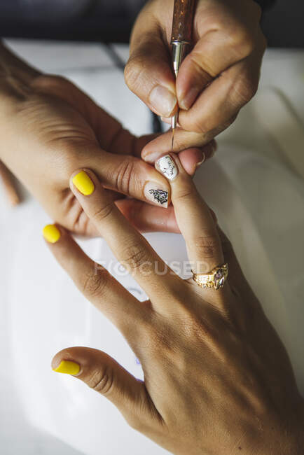 Зверху врожаю невпізнаваний манікюрник займається мистецтвом нігтів для жіночого клієнта в салоні краси в денний час — стокове фото