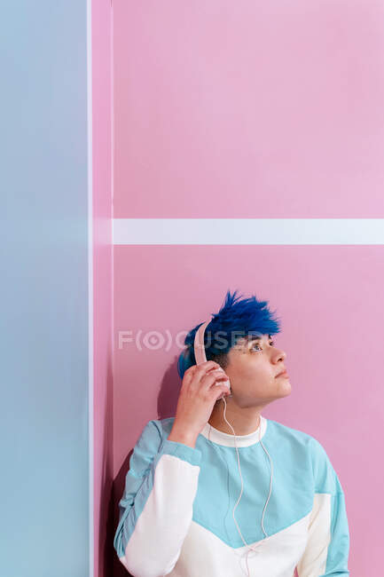 Giovane donna contemplativa con i capelli blu che ascolta la canzone dalle cuffie mentre alza lo sguardo su tre colori di sfondo — Foto stock