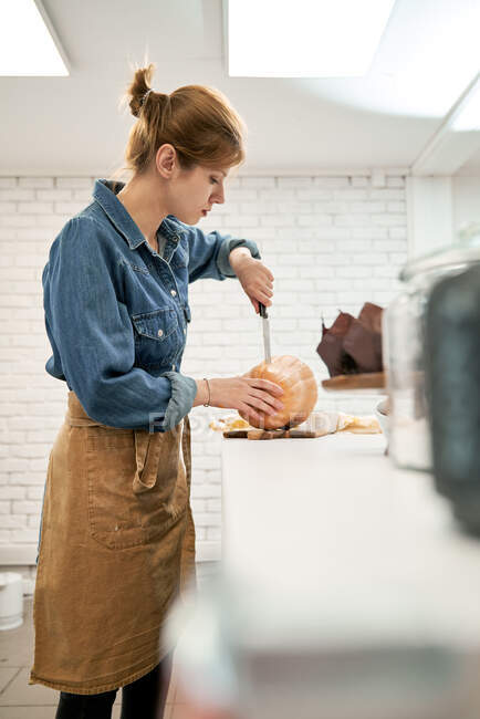 Giovane femmina con coltello affilato taglio zucca cruda sul tagliere durante la cottura in cucina a casa — Foto stock