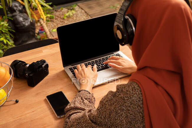 Сверху анонимная женщина в платке, используя современный нетбук с черным экраном, сидя за столом — стоковое фото