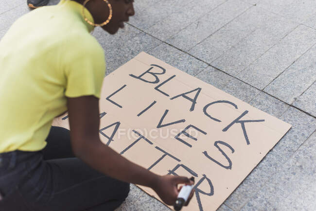 High angle side view of cropped African American female activist writing Black Lives Matter and making placard for protest against racism in city — Photo de stock