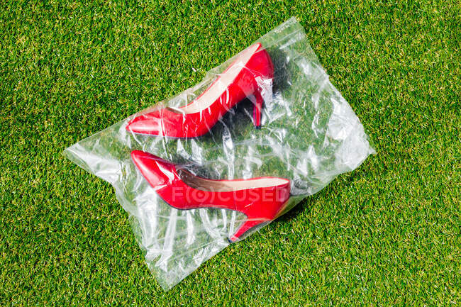 Vue du dessus de la paire de chaussures rouges dans un sac en plastique placé sur une pelouse verte — Photo de stock