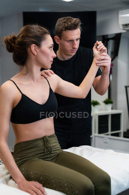 Male physical therapist examining shoulder and arm joint mobility of female patient on bed in hospital — Stock Photo