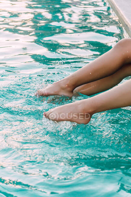 Crop anonymous barefoot female travelers touching shiny rippled water in swimming pool during trip — Stock Photo