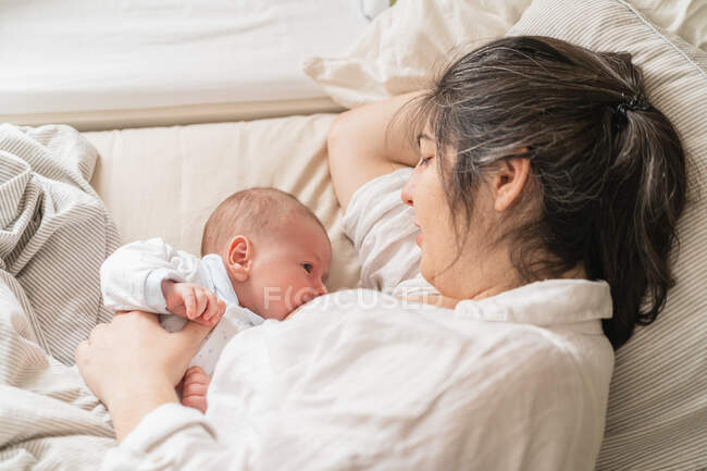 Hohe Winkel der erwachsenen Mutter saugt entzückendes Baby, während sie auf dem Bett liegt und einander ansieht — Stockfoto