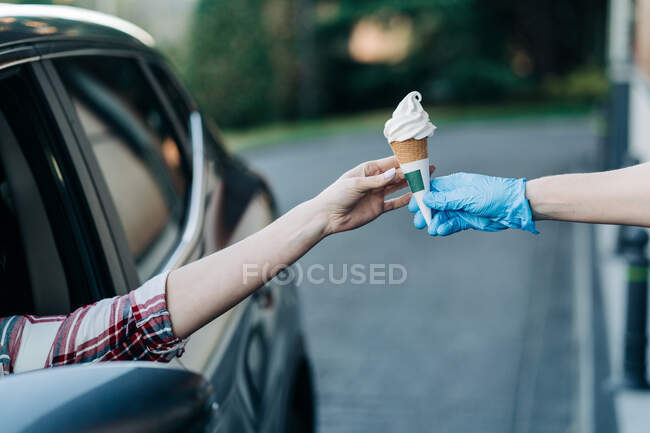 Врожай невпізнавана жінка сидить в машині і приймає морозиво в проїзді через кафе в місті — стокове фото