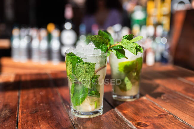 Glasses of refreshing mojito cocktails with ice and mint served on outdoor wooden bar counter — Stock Photo