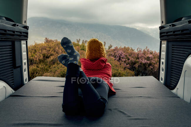 Back view of unrecognizable traveling teenager lying in van and enjoying view of highlands during trip — Stock Photo
