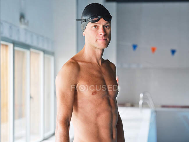 Masculino nadador em óculos profissionais com corpo muscular em pé antes do treinamento em luz solar no fundo embaçado olhando para a câmera — Fotografia de Stock