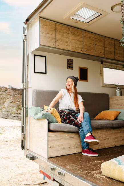 Seitenansicht von glücklich reisenden Hipsterinnen, die auf der Couch im LKW sitzen und Urlaub am See genießen — Stockfoto