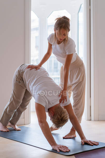 Man practicing yoga in Downward Facing Dog pose with help of female instructor during session at home — Stock Photo