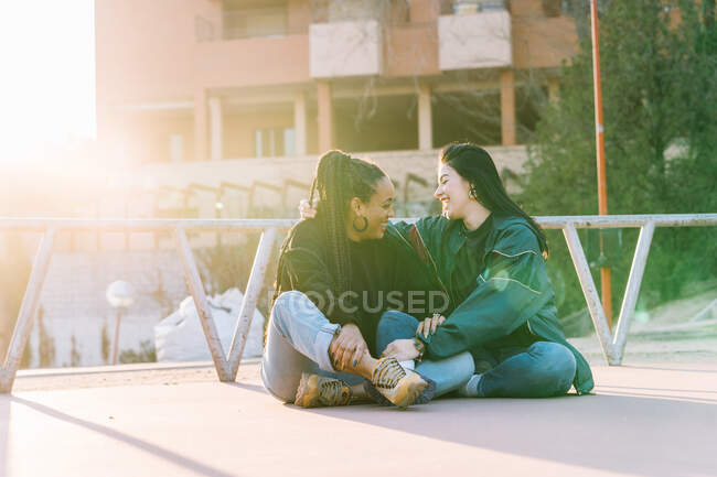Inhalt multiethnische homosexuelle Freundinnen mit überkreuzten Beinen, die sich an einem sonnigen Tag in der Stadt anschauen — Stockfoto