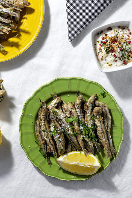 From above of fried and canned anchovies served on table with fresh lemons in restaurant in sunlight — Photo de stock