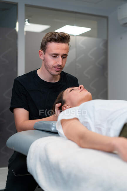 Unshaven fisioterapeuta masculino massageando pescoço de mulher com olhos fechados no hospital — Fotografia de Stock